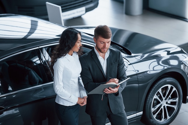 Remplir les documents. Clientèle féminine et homme d'affaires barbu élégant et moderne dans le salon automobile