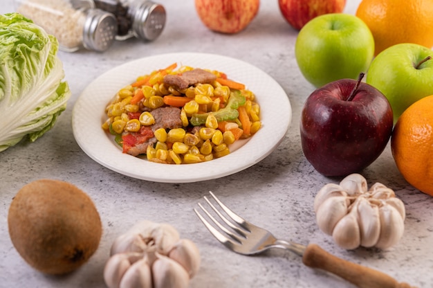 Remuez le maïs et les carottes, mettez le porc dans l'assiette sur l'assiette en bois.