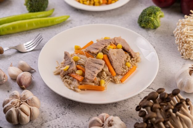 Remuez le maïs et les carottes, mettez le porc dans l'assiette sur l'assiette en bois.