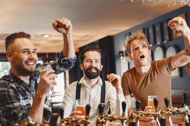 Rencontre avec les meilleurs amis. trois jeunes hommes heureux en tenue décontractée parlant et buvant de la bière assis ensemble au bar.