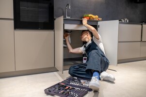 Réparation de ménage homme d'âge moyen inspectant le tuyau touchant la main sous l'évier dans une cuisine moderne et élégante