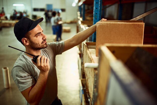 Répartiteur masculin vérifiant les colis tout en utilisant le talkie-walkie dans l'entrepôt de distribution