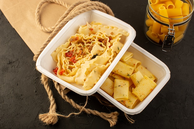 Un repas de pâte vue de dessus avec des herbes vertes séchées à l'intérieur de bols blancs et de l'emballage sur dark