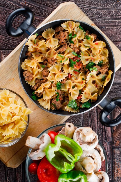 Repas de pâtes dans une poêle avec des pâtes crues, des champignons, du poivre, de la tomate