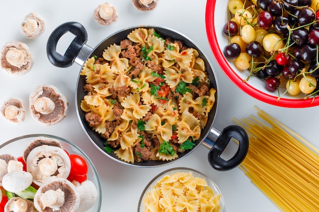 Repas de pâtes dans une poêle avec des pâtes crues, champignons, poivrons, tomates, cerises