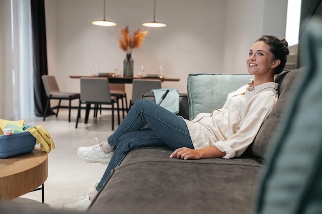 Repos. Souriante jeune femme assise à la maison sur le canapé