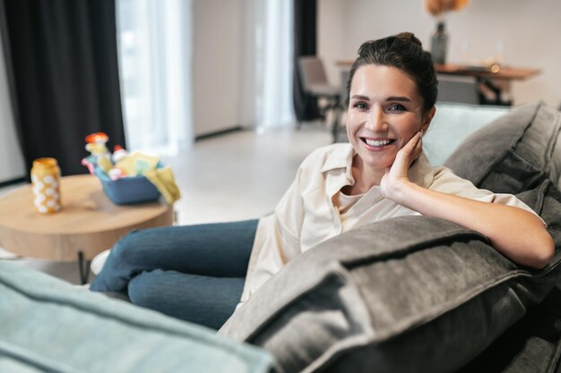 Repos. Souriante jeune femme assise à la maison sur le canapé