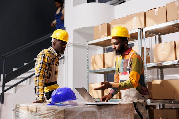 Photo gratuite des responsables de la logistique afro-américains discutent d'un logiciel de gestion des stocks tout en vérifiant les marchandises en stock sur leur ordinateur portable.