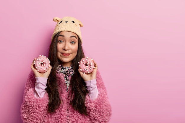 Restauration rapide, concept de mauvaise alimentation. Des poses féminines attrayantes avec de délicieux beignets, suggèrent de goûter des confiseries maison, ont la dent sucrée, portent des vêtements d'extérieur. Ton pastel