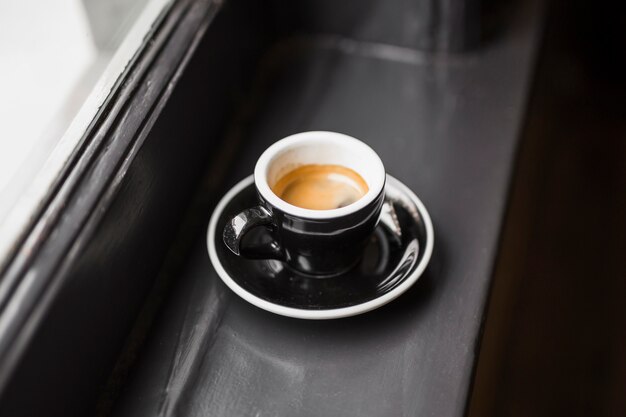 Reste de café dans une tasse noire sur le rebord de la fenêtre