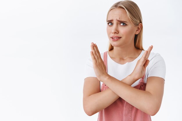 Reste loin de moi, recule. Jeune femme blonde effrayée et mécontente aux yeux bleus, aux tatouages, se croisant et regardant avec panique, alarmée, fronçant les sourcils dérangée, refusant ou rejetant l'offre