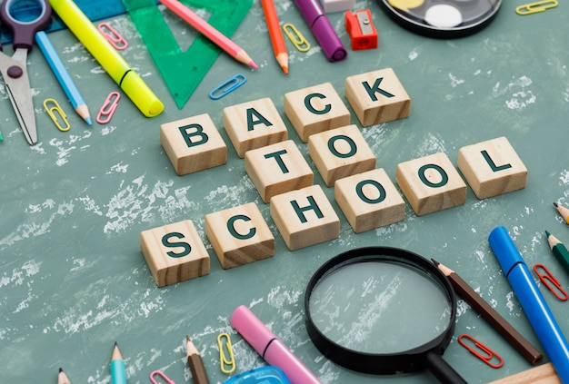 Retour au concept de l'école avec des cubes en bois, loupe, fournitures scolaires sur fond de plâtre vue en plongée.