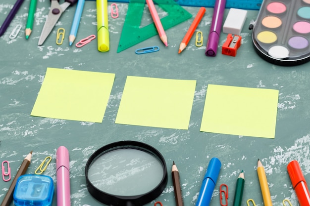 Retour au concept de l'école avec des notes autocollantes, loupe, fournitures scolaires sur fond de plâtre vue en plongée.