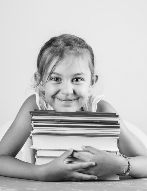 Retour au concept de l'école sur le plâtre et vue latérale du mur blanc. petite fille étreignant des cahiers et des livres.