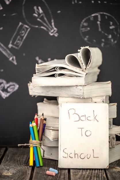 Retour à l'école, pile de livres et fournitures scolaires sur fond de tableau noir peint à la craie, concept de l'éducation