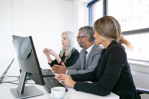 Réunion des chefs d'entreprise. Équipe de professionnels assis sur le lieu de travail avec des moniteurs ensemble et discutant du projet. Vue de côté. Concept de réunion d'affaires