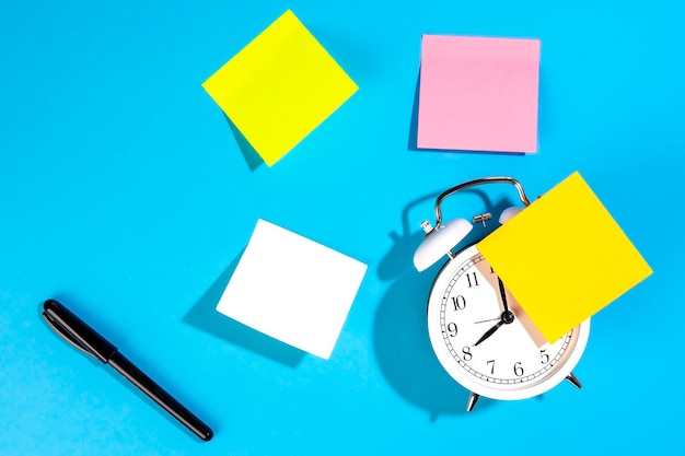 Réveil et rappels de papier vierge coloré sur une vue de dessus de fond bleu