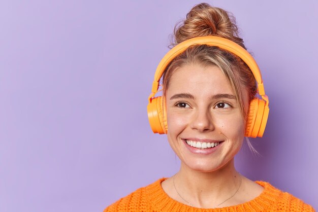 Rêveuse belle jeune femme sourit largement aime la piste audio dans les écouteurs sans fil concentrée avec une expression rêveuse isolée sur fond violet espace vide vide pour votre promotion