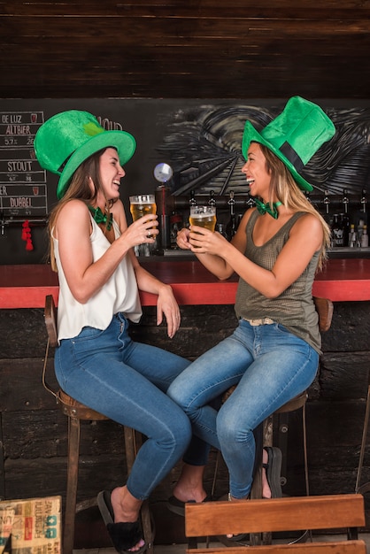 Rire des femmes en chapeaux Saint Patrick avec des verres de boisson au comptoir