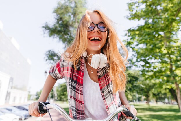 Rire fille enchanteresse posant dans le parc. Excité dame dans des vêtements décontractés exprimant le bonheur en journée d'été.