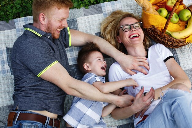 Rire jeune famille se trouve sur le plaid dans le parc