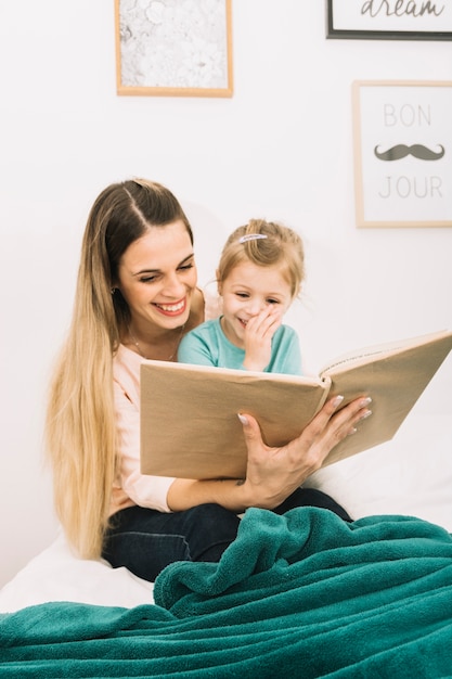 Rire mère et fille lisant un livre sur le lit