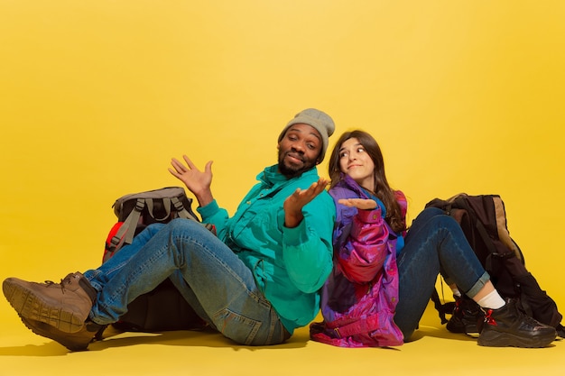 Rire. Vrais amis. Portrait d'un jeune couple de touristes joyeux avec des sacs isolés sur fond de studio jaune. Se préparer au voyage. Resort, émotions humaines, vacances, amitié, amour.