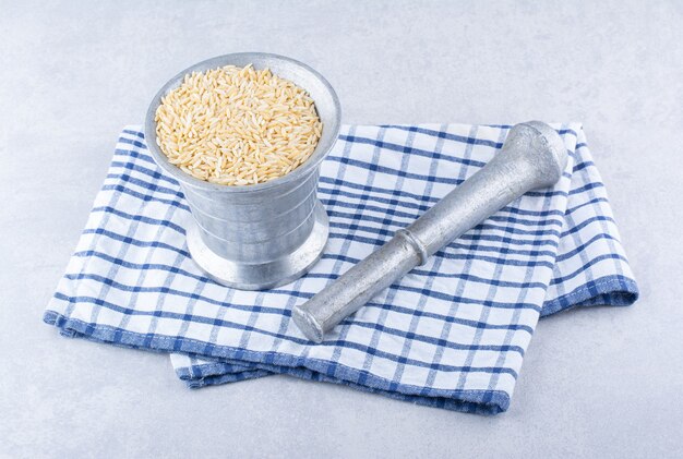 Photo gratuite riz brun dans une cruche en métal à côté d'un presse-purée sur une serviette pliée sur une surface en marbre