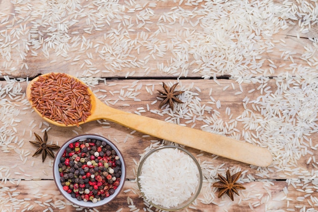 Photo gratuite riz brun dans une cuillère en bois avec du poivre et l'anis étoilé sur le fond en bois rustique