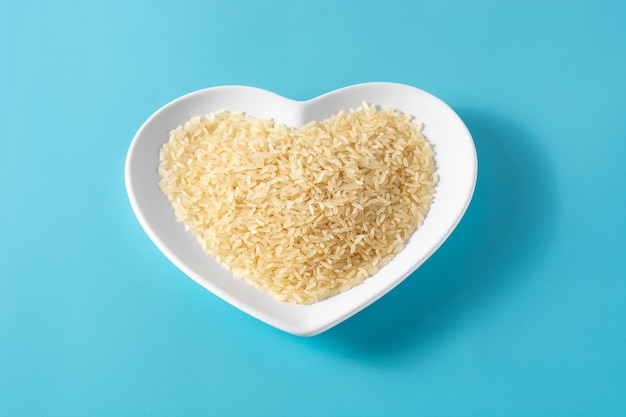 Riz cru sur plaque en forme de coeur sur fond bleu