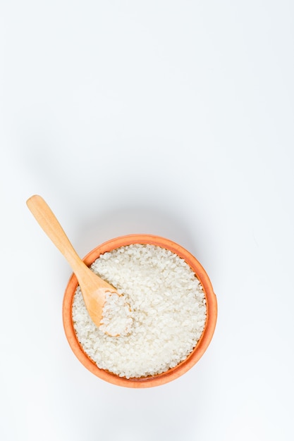 Riz frais dans un bol en bois avec une vue de dessus de cuillère en bois sur fond blanc