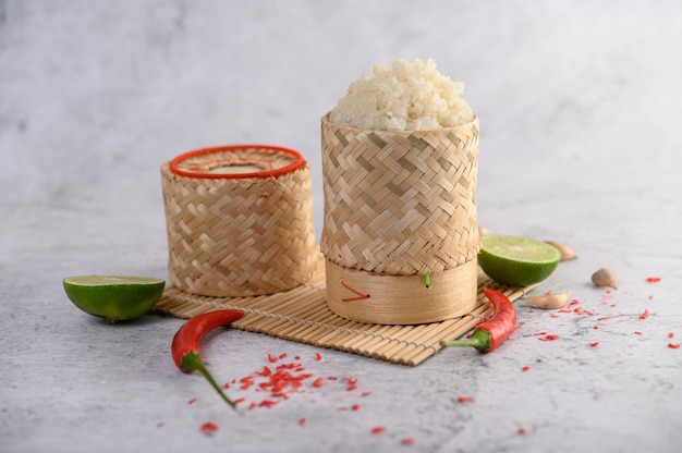 Riz gluant thaï dans un panier en bambou tressé sur un panneau en bois avec des piments, du citron vert et de l'ail