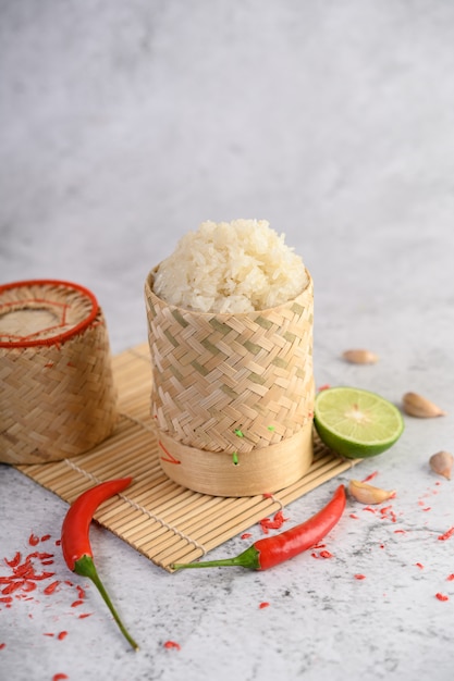 Riz gluant thaï dans un panier en bambou tressé sur un panneau en bois avec des piments, du citron vert et de l'ail