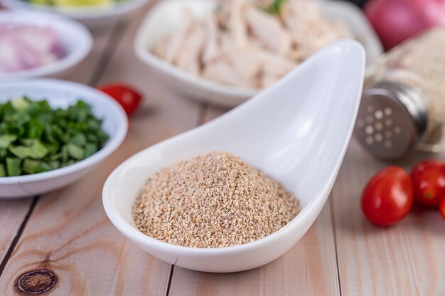 Riz rôti dans une cuillère blanche, tomate posée sur une table en bois.