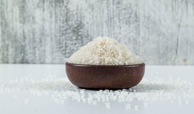 Photo gratuite riz sec sec dans un bol sur fond blanc et grunge. vue de côté.