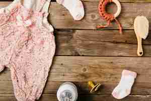 Photo gratuite robe de bébé; brosse; sucette; jouet; chaussettes et bouteille de lait sur une table en bois