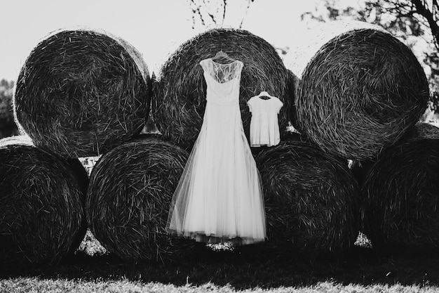 Photo gratuite robe de mariée longue et petite robe pour enfant accroche sur des rouleaux de foin