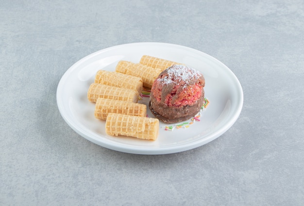 Rôles de gaufres en tranches sucrées avec gâteau sur une assiette blanche.