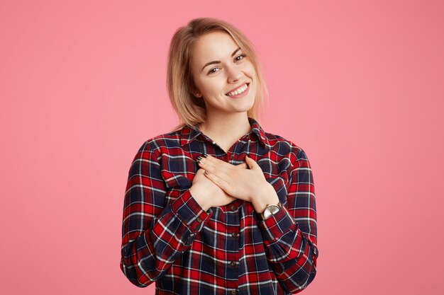 Romantique belle jeune femme avec un agréable sourire brillant, garde les mains sur la poitrine