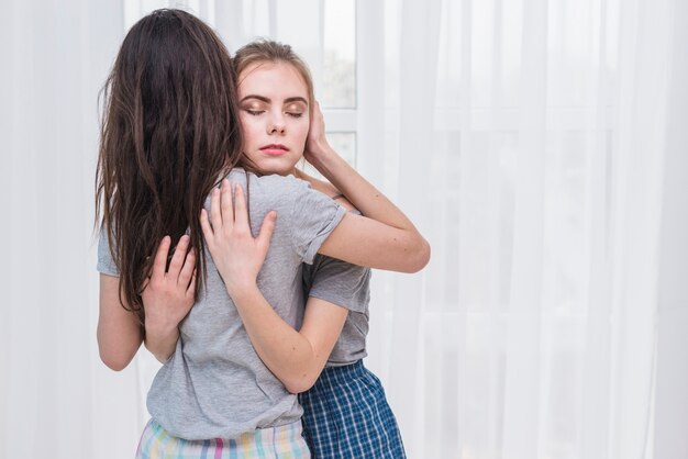 Romantique jeune couple de lesbiennes s&#39;embrassant debout près de la fenêtre