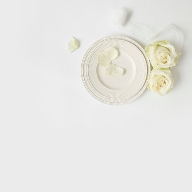 Rose; ruban blanc et assiettes sur fond blanc