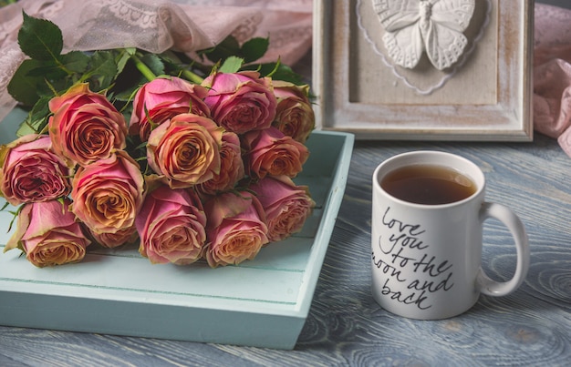 Roses roses et une tasse de thé blanche avec citation d'amour sur elle