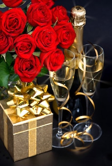 Roses rouges, champagne et cadeau doré sur fond noir. décoration de fête