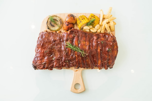 Photo gratuite rôti de porc grillés avec sauce barbecue et légumes et frites sur planche à découper en bois