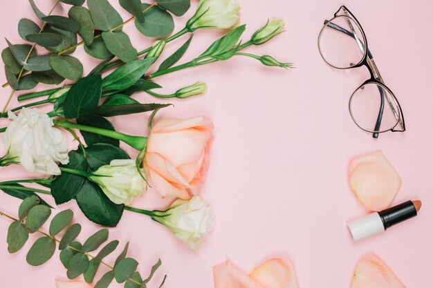 Rouge à lèvres; lunettes et bouquet de fleurs sur fond rose