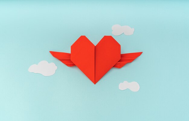 Rouge papier origami coeur avec des ailes et des nuages ​​sur fond bleu