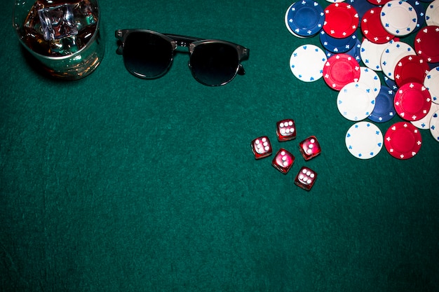 Photo gratuite dés rouges; jetons de casino; verres à whisky et lunettes de soleil sur fond de poker vert