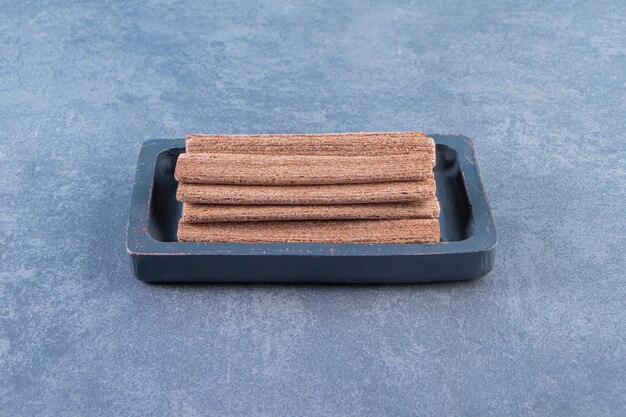 Rouleau de gaufrettes au chocolat savoureux dans une assiette en bois sur la surface en marbre