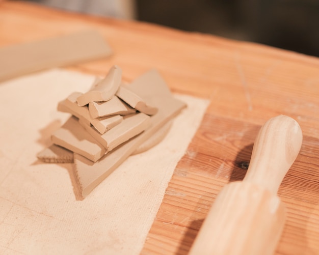 Un rouleau à pâtisserie et une pile d&#39;argile humide de différentes formes sur un bureau en bois