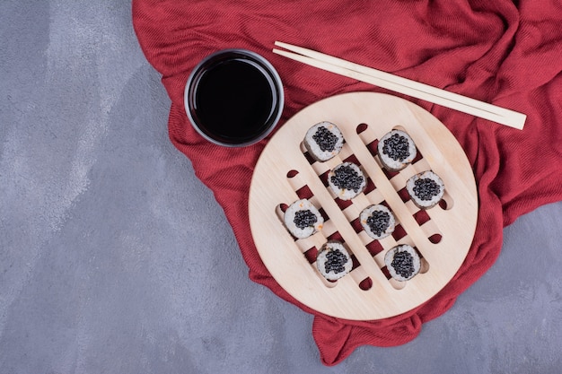 Rouleau de sushi maki traditionnel avec des baguettes et de la sauce soja sur une nappe rouge.